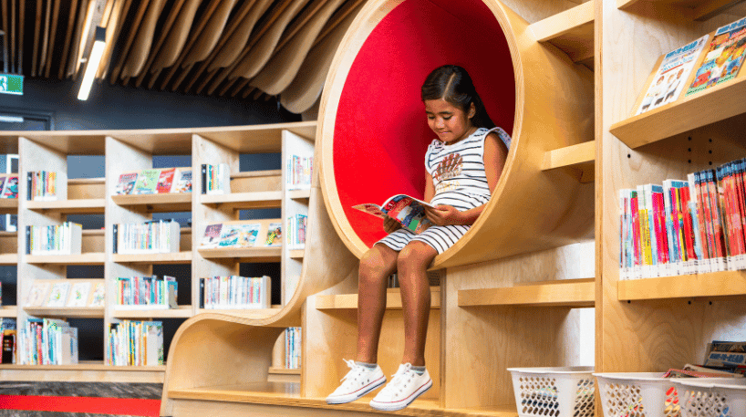 Girl seated on a bookshelf reading