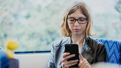 Young woman reading using a mobile device and headphones on the train.